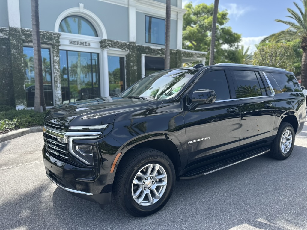 Black Chevrolet Suburban parked beside landscaped grounds and flags.
