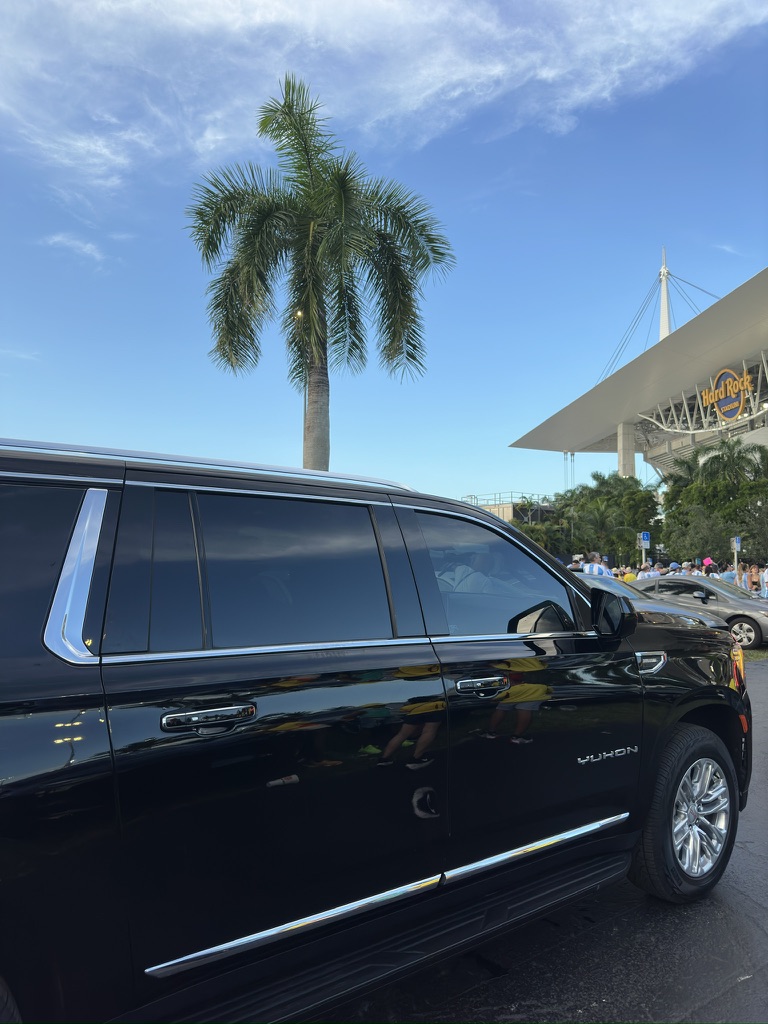 Black GMC Yukon outside Hard Rock Stadium, with palm trees and spectators in the background.